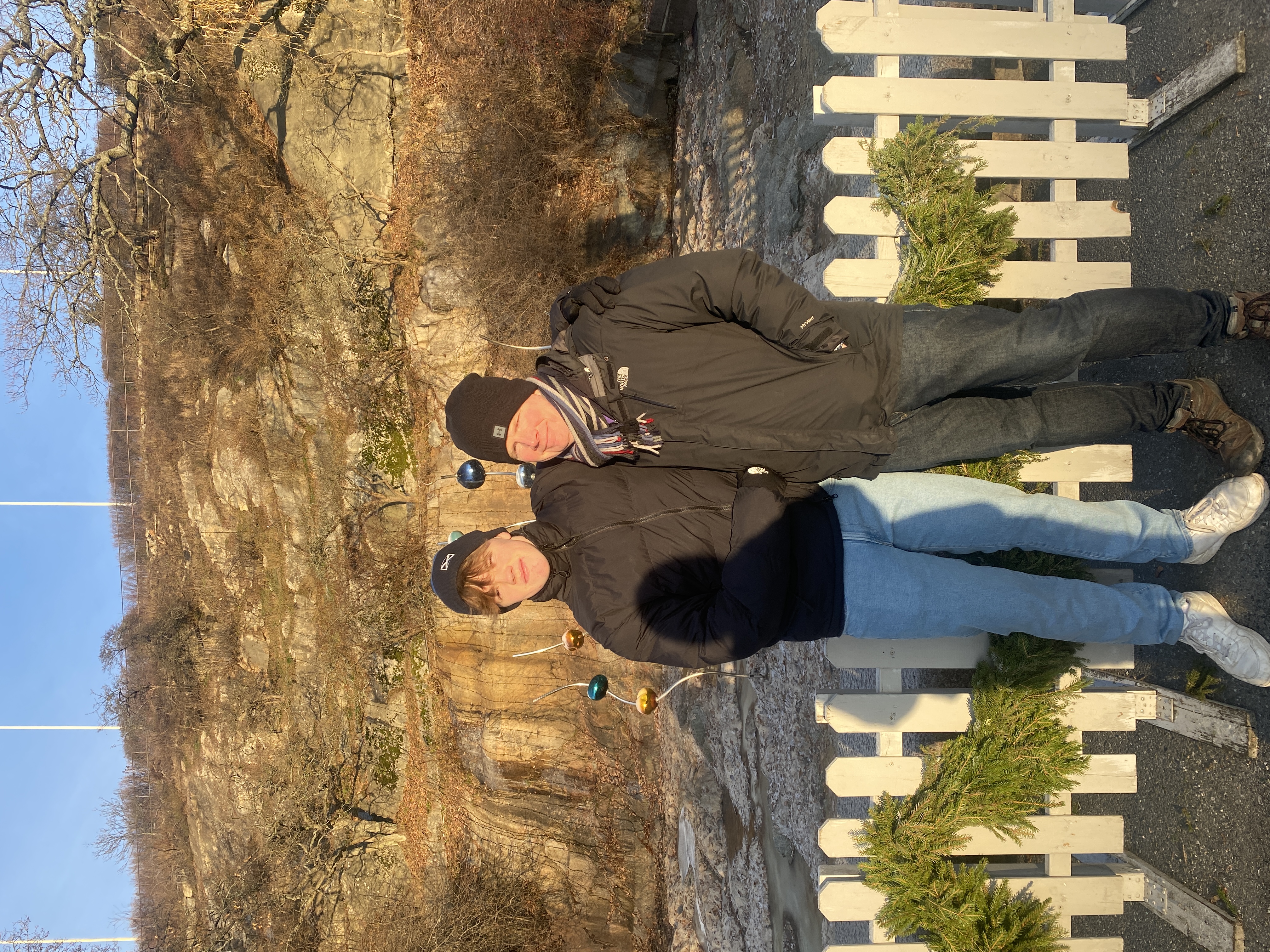 Two men posing on a sunny day in front of a cliff wearing warm clothes.